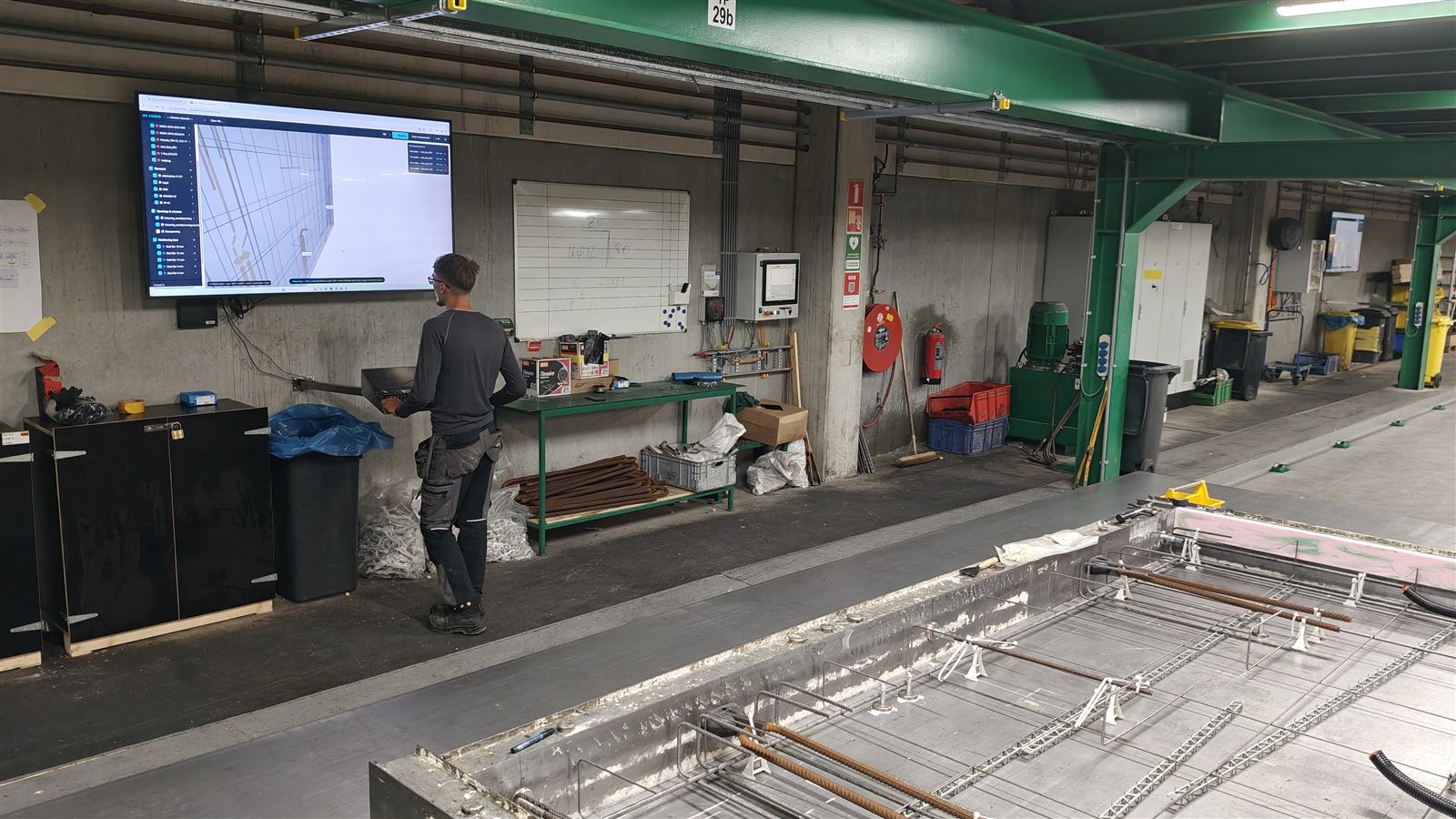 Operator at the production line of a precast plant using the IFC viewer on a large wall screen, next to a mould with rebar